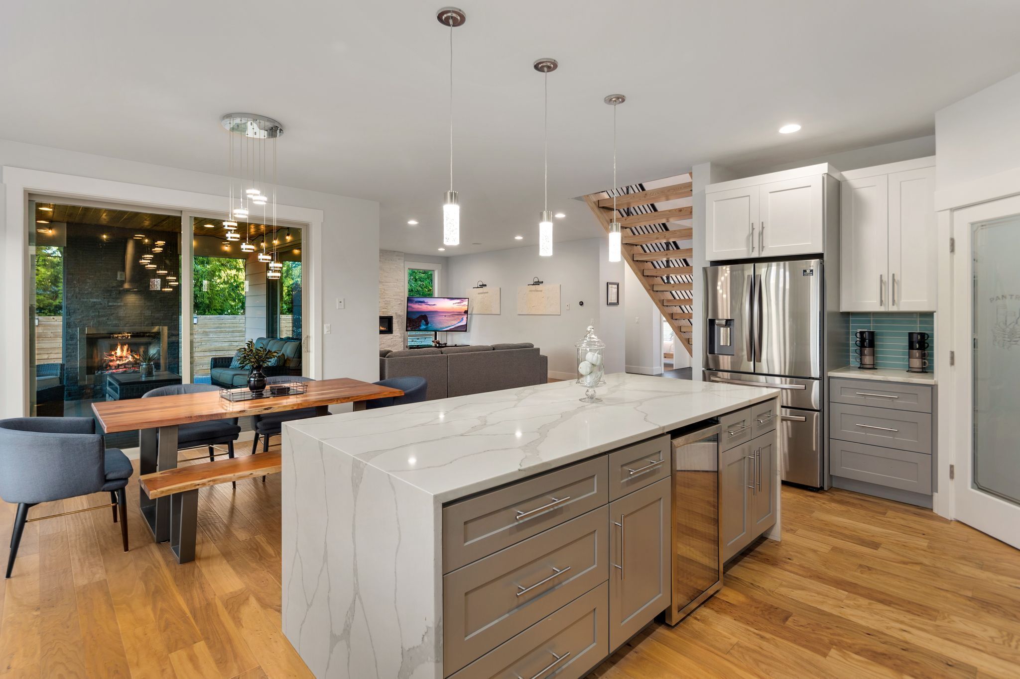 A modern kitchen with a marble island, stainless steel appliances, and a wooden staircase.