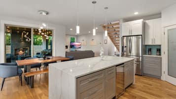A modern kitchen with a marble island, stainless steel appliances, and a wooden staircase.
