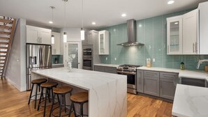 Une cuisine moderne dotée d’un grand îlot central, de tabourets de bar, d’appareils électroménagers en acier inoxydable et de carreaux de crédence de couleur turquoise.