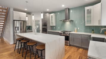 A modern kitchen with a large island, bar stools, stainless steel appliances, and teal backsplash tiles.