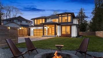 A modern two-story house with a fire pit in the backyard, outdoor seating, and a well-maintained lawn.