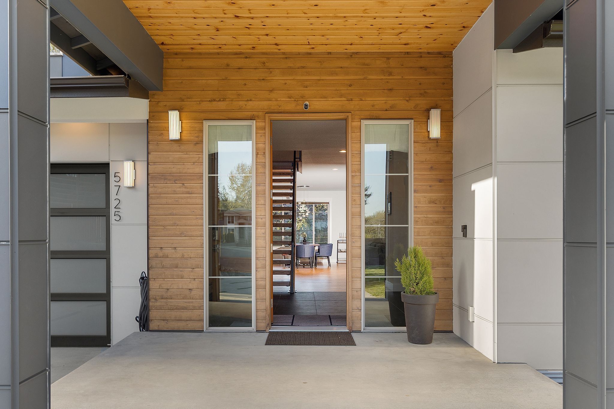 A modern building entrance with a wooden ceiling, glass doors, and a visible staircase inside.