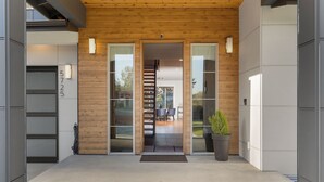 Une entrée moderne avec un plafond en bois, des portes en verre et un escalier visible à l’intérieur.