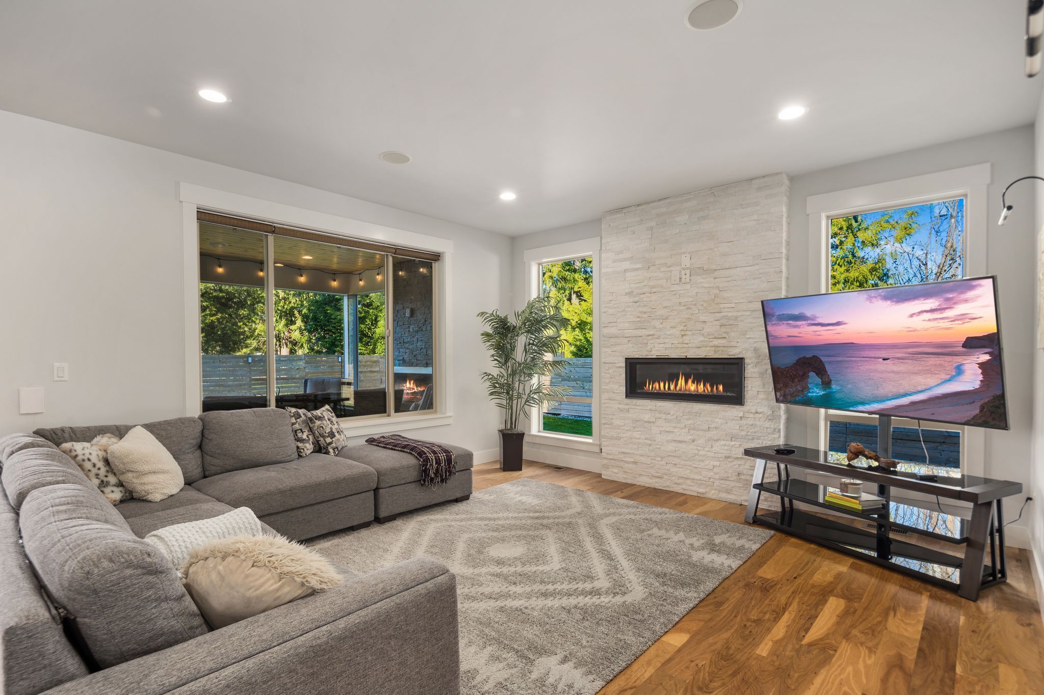 A modern living room with a grey sectional sofa, a fireplace, a large flat-screen TV, and a stone accent wall.