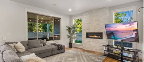 A modern living room with a grey sectional sofa, a fireplace, a large flat-screen TV, and a stone accent wall.