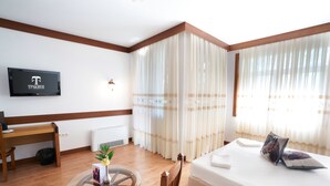 A hotel room with a bed, a TV mounted on the wall, a wooden desk, and a glass table with a vase of flowers. - Boutique Complex Trakiets (Kaloyanovo)