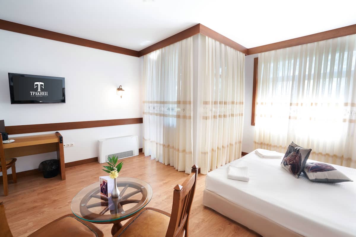 A hotel room with a bed, a TV mounted on the wall, a wooden desk, and a glass table with a vase of flowers.