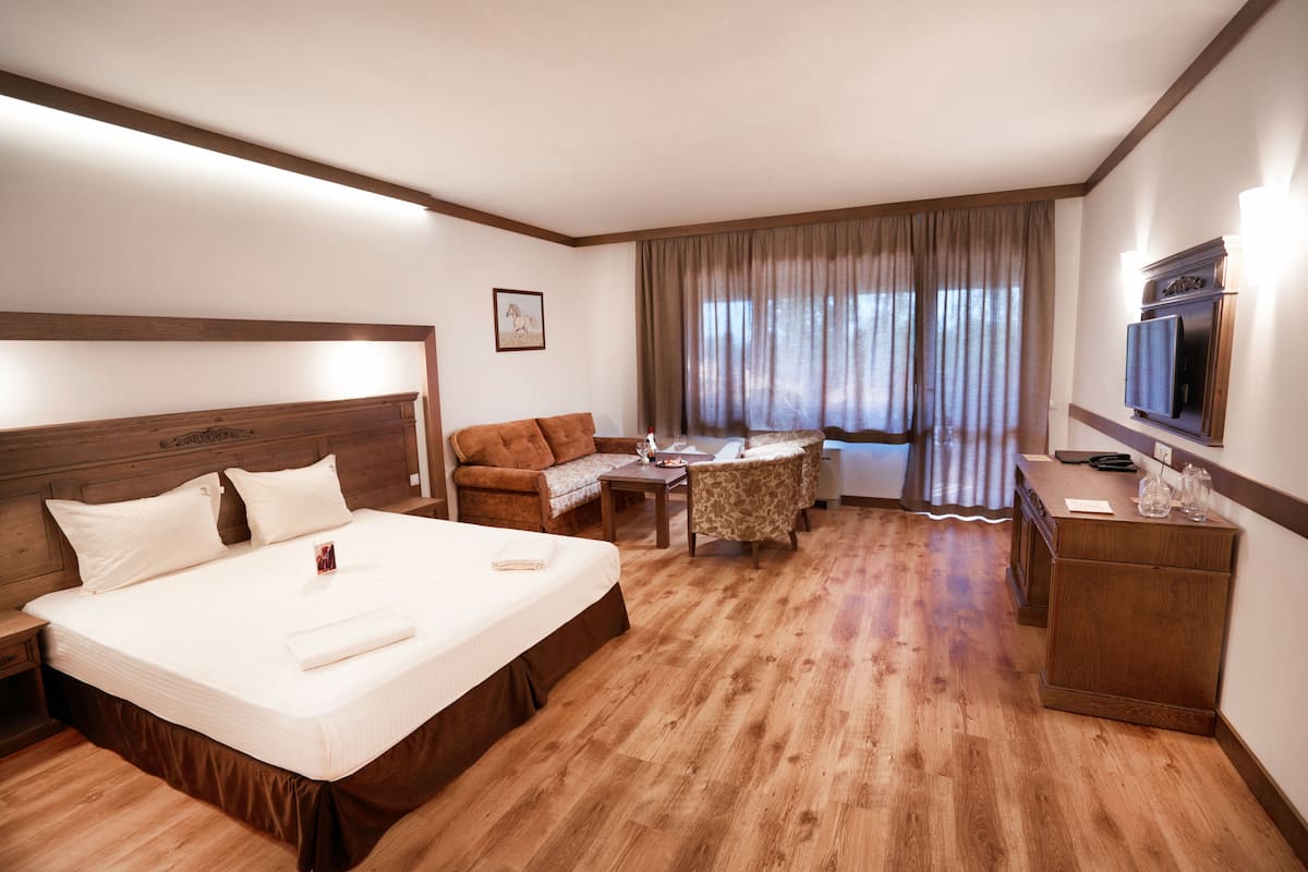 A hotel room with a large bed, a sofa, a small table, a TV, and a wooden dresser.