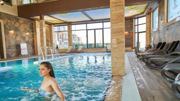 An indoor swimming pool with a person in the water, lounge chairs, and a stone wall. - Boutique Complex Trakiets (Kaloyanovo)