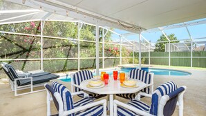 Une terrasse couverte avec une piscine, des chaises à rayures et une table avec des boissons.