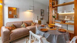 A cozy living room with a brown sofa, a dining table set with plates and glasses, and a wooden shelf with various items. - Spacious apartment with WiFi at the foot of the slopes - La Daille (Val-d'Isère)
