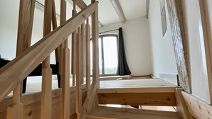 Una escalera de madera conduce a un dormitorio en el ático, con ventana y vistas al exterior.
