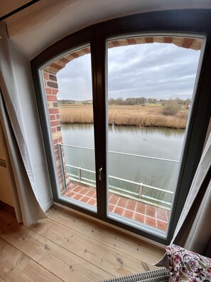 Een kamer met een groot raam met uitzicht op een waterpartij en een veld.
