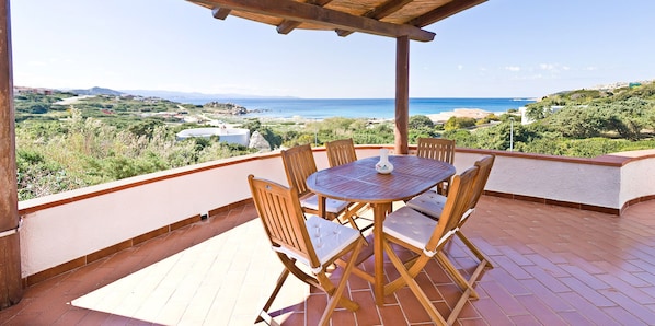 A covered patio with a table and chairs, overlooking a coastal landscape.
