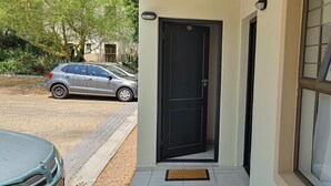 Une porte noire avec une plaque portant un numéro, une voiture garée devant, et une fenêtre donnant sur la rue.
