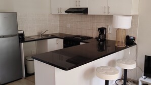 Une cuisine compacte équipée d’un réfrigérateur, d’une cuisinière, d’un évier et de deux tabourets de bar.