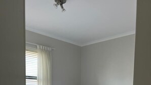 Un lit bien fait, avec du linge de lit blanc et une serviette enroulée, une lampe de chevet et une fenêtre avec des stores.