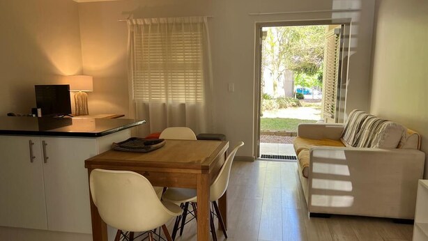 Un espace de vie compact comprenant un coin repas, un canapé et une porte-fenêtre coulissante donnant sur un jardin.