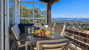 An outdoor patio with a table set for a meal, featuring a bottle of wine, glasses, and a fruit basket.