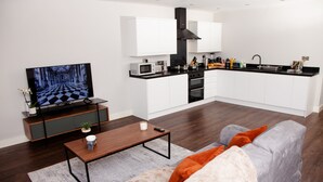 A modern living room with a flat-screen TV, a wooden coffee table, and a grey sofa with orange cushions. - High Life Luxury Serviced Apartments  (Swindon)
