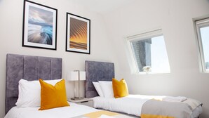 A hotel room with two beds, a window, and two framed pictures on the wall. - High Life Luxury Serviced Apartments  (Swindon)