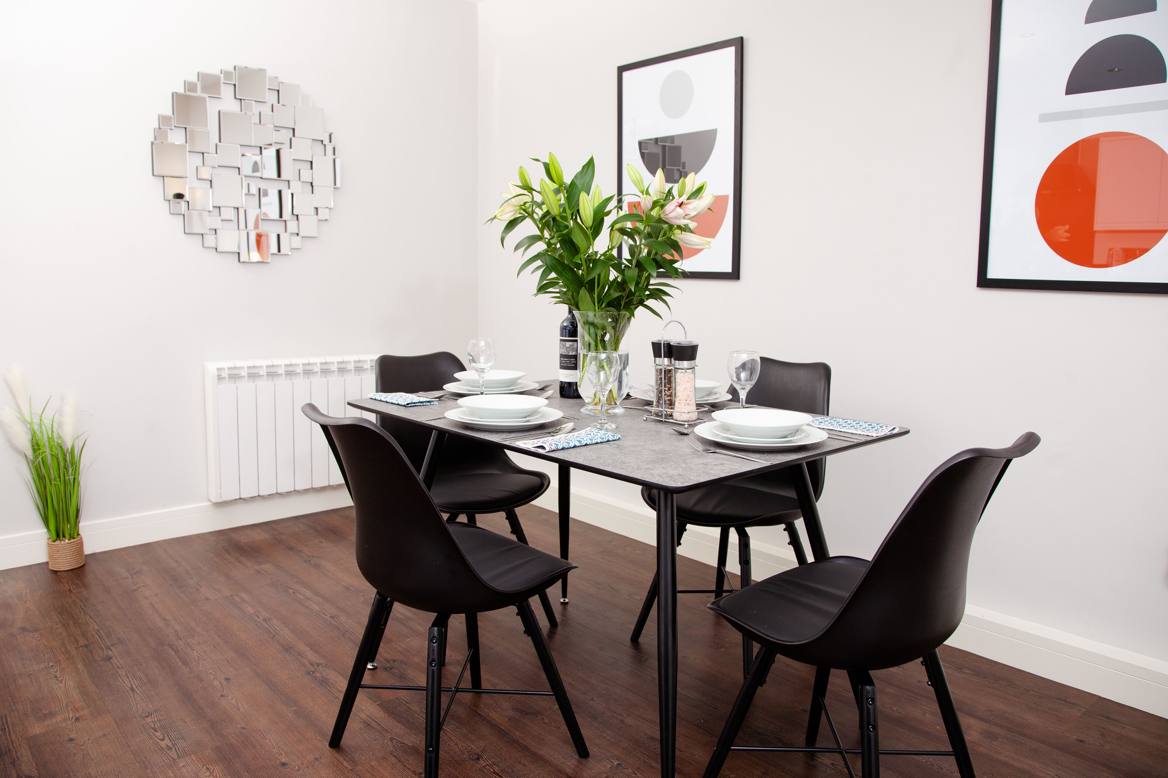 A dining area with a rectangular table, black chairs, white plates, and a vase with flowers.