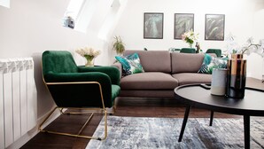 A modern living room with a green armchair, a brown sofa, and a round coffee table. There are framed botanical prints on the wall and a plant on the table. - High Life Luxury Serviced Apartments  (Swindon)