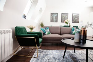 Una sala de estar moderna con un sillón verde, un sofá marrón y una mesa de centro redonda. Hay impresiones botánicas enmarcadas en la pared y una planta sobre la mesa.