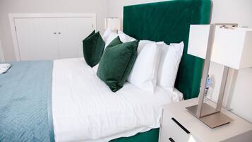 Un letto rifatto con lenzuola bianche e verdi, un comodino con una lampada e un armadio bianco in una camera d'albergo.