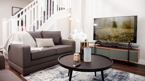 A modern living room with a grey sofa, a round coffee table, and a flat-screen TV. - High Life Luxury Serviced Apartments  (Swindon)