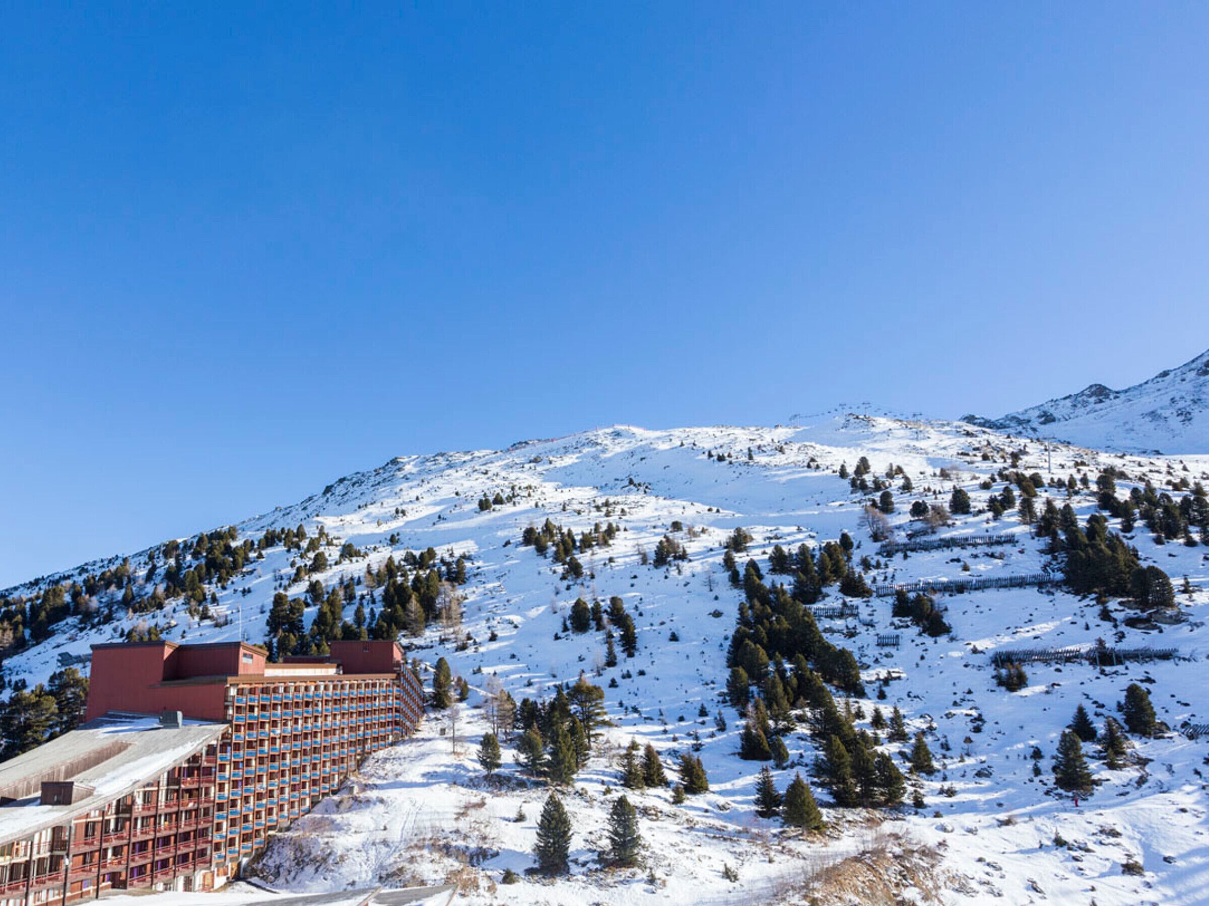 Ein Hotel mit einem roten Gebäude und mehreren Stockwerken, umgeben von schneebedeckten Bergen und Bäumen.