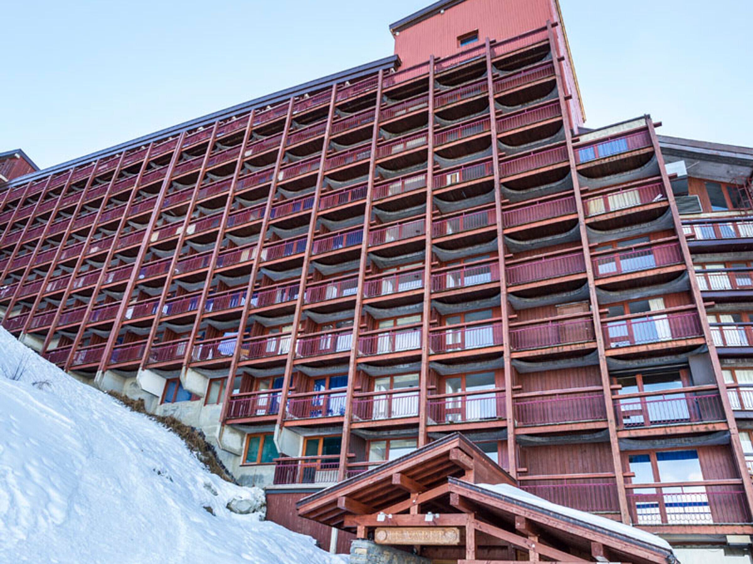 Un hotel de varios pisos con balcones y una pista de esquí al fondo.