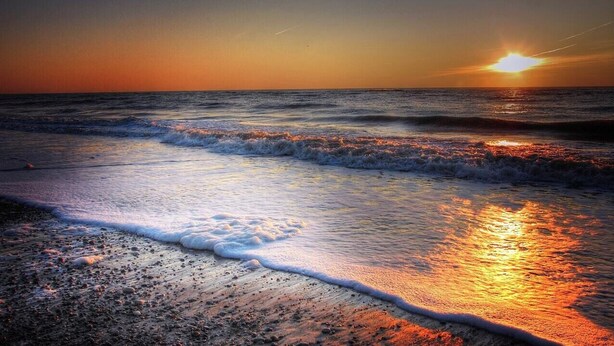 Ein Strand bei Sonnenuntergang, wo sanfte Wellen an das Ufer rollen.