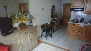 Une cuisine compacte avec un coin repas, un téléviseur posé sur un meuble et un vase avec des fleurs.