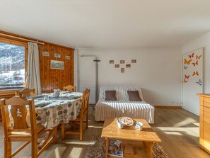 A cozy room with a wooden dining table set for two, a single bed with a striped blanket, and a window with a view of a snowy landscape. - South studio ski-in/ski-out in Val-d'Isère, pets allowed (Val-d'Isère)