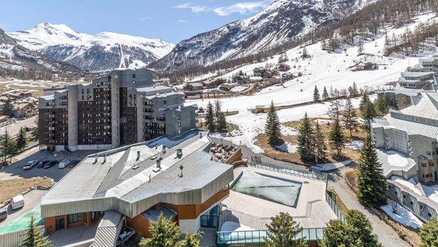 A modern hotel with a unique architectural design, situated in a mountainous area with snow-covered peaks in the background. - South studio ski-in/ski-out in Val-d'Isère, pets allowed (Val-d'Isère)