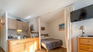 A compact hotel room with a kitchenette, a bed, a TV, and a wooden dresser. - South studio ski-in/ski-out in Val-d'Isère, pets allowed (Val-d'Isère)