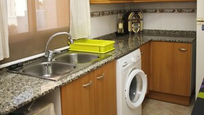 A kitchen with granite countertops, wooden cabinets, a stainless steel sink, a washing machine, and a coffee maker.