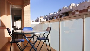 A balcony with a round table and four chairs, a tiled floor, and a white partition wall.
