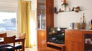 A living room with a TV, wooden cabinet, and a dining area with chairs.
