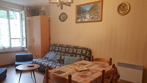 A cozy living room with a patterned sofa, a small round table, and a dining table with chairs. - Apartment 4 People Center Cauterets (Cauterets)