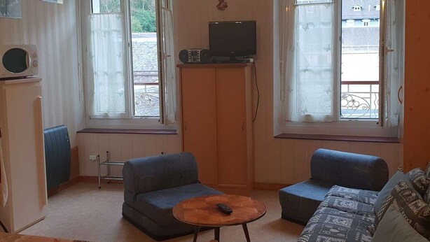 A small living room with two blue sofas, a wooden coffee table, a television on a wooden stand, and a window with a view of the outside. - Apartment 4 People Center Cauterets (Cauterets)
