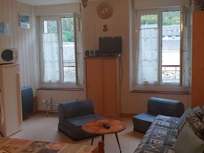 A small living room with two blue sofas, a wooden coffee table, a television on a wooden stand, and a window with a view of the outside. - Apartment 4 People Center Cauterets (Cauterets)