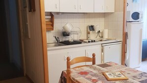 A compact kitchen with white cabinets, a stove, a microwave, and a sink. - Apartment 4 People Center Cauterets (Cauterets)