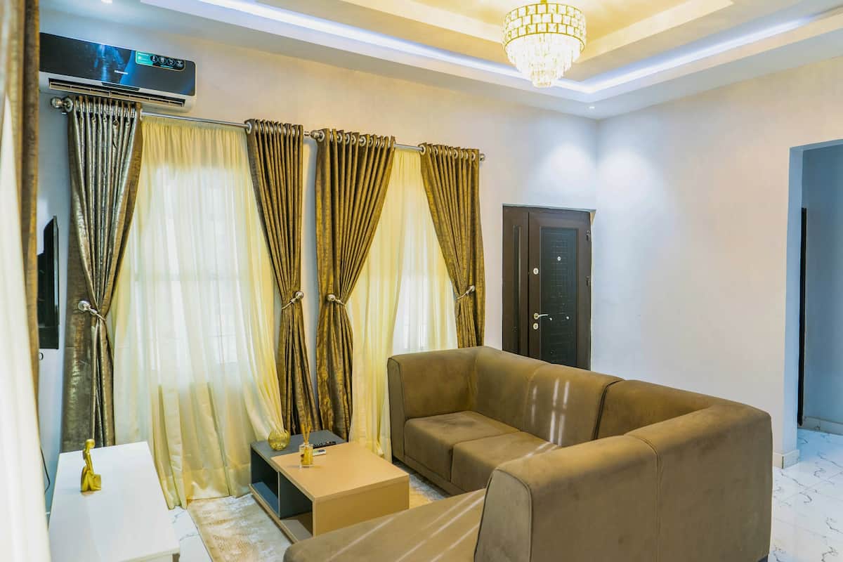 A living room with a sofa, curtains, a door, and a chandelier.