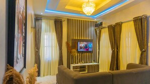 A living room with a sofa, TV, and curtains. - Grey Top Apartment (Abuja)