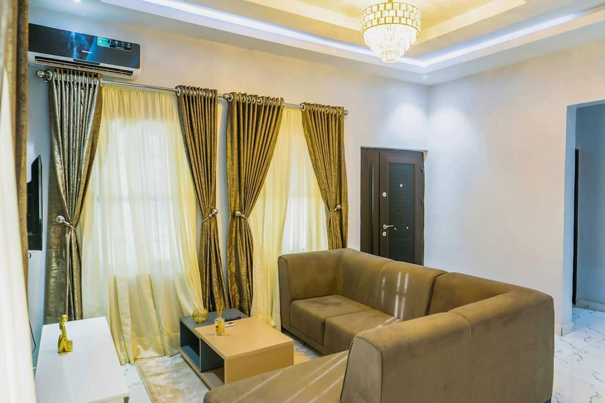 A living room with a sofa, curtains, a door, and a chandelier.