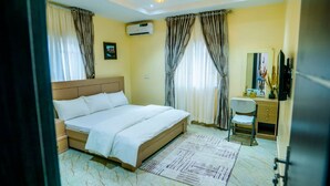 A hotel room with a bed, a desk, a chair, a mirror, and an air conditioning unit. - Grey Top Apartment (Abuja)