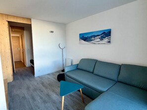 En moderne stue med sofa, et lille bord, en radiator og en dør til et andet rum.