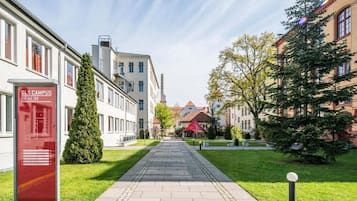 Ein Weg führt zu einem Gebäude mit der Aufschrift "GLS Campus Berlin", mit einem roten Briefkasten, umgeben von Grünflächen und traditioneller Architektur.